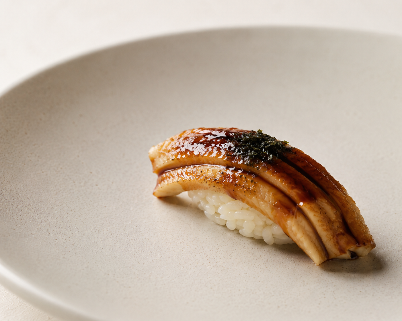 Anago sea eel nigiri with tare glaze and toasted nori on a matte ceramic plate