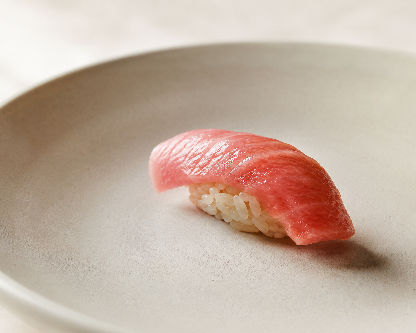 A single piece of otoro nigiri resting on a pale matte ceramic plate