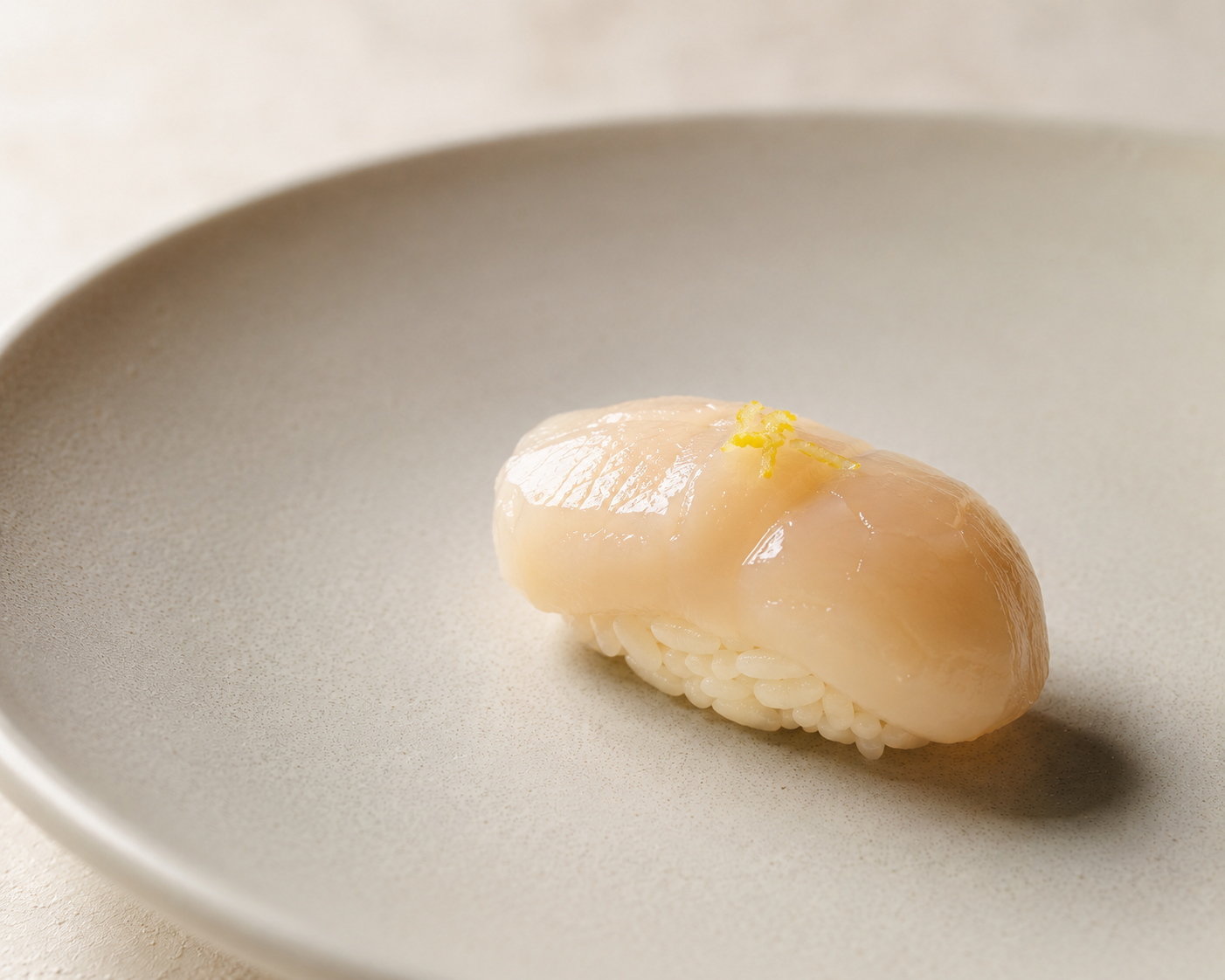Hotate scallop nigiri with yuzu on a matte ceramic plate