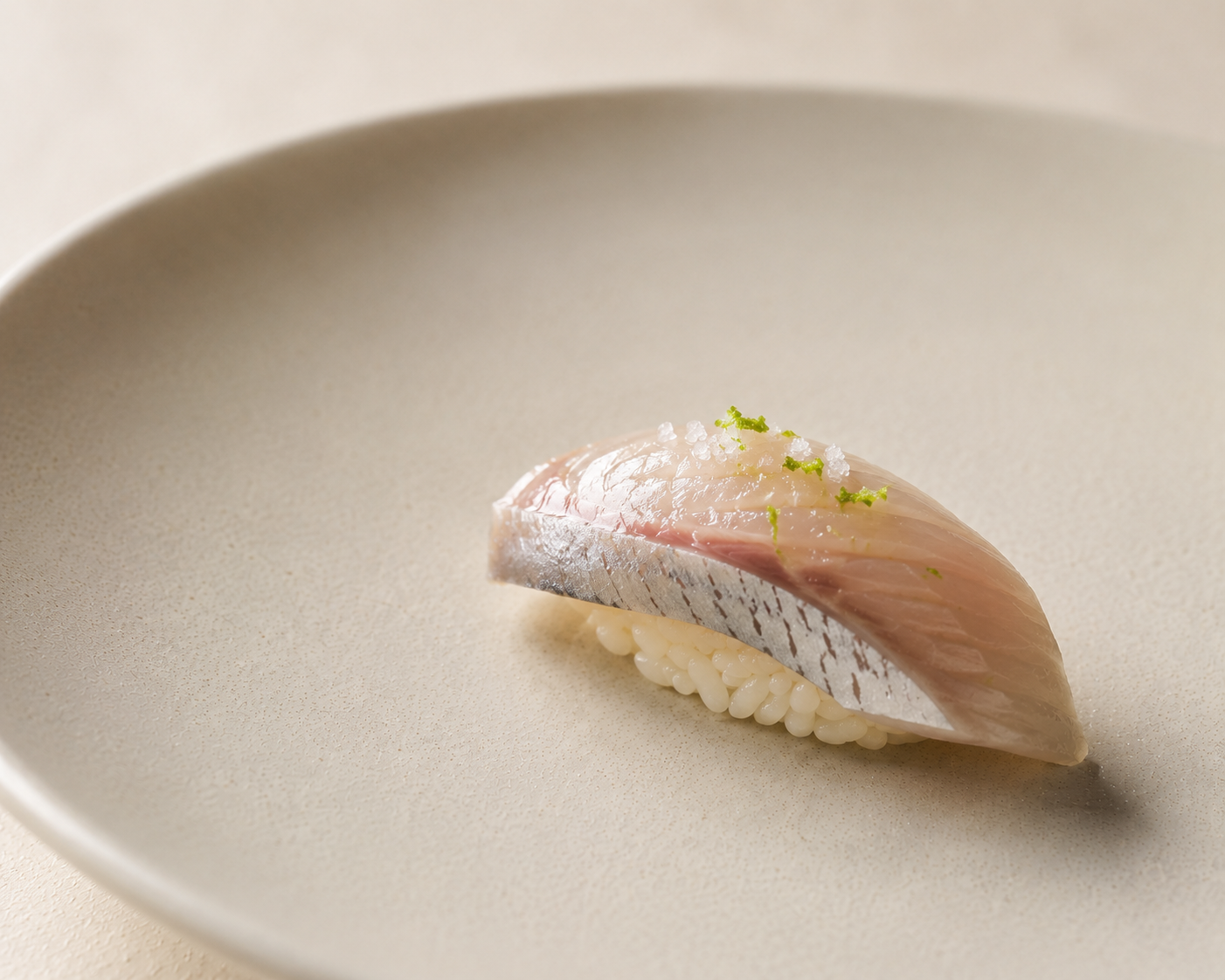 Shima aji nigiri with citrus zest and sea salt on a matte ceramic plate
